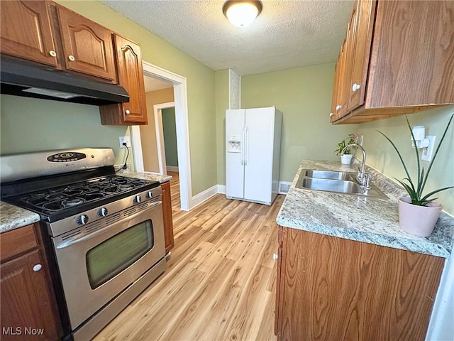 kitchen featuring a textured ceiling, sink, white refrigerator with ice dispenser, light hardwood / wood-style floors, and stainless steel range with gas cooktop