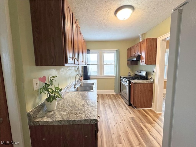 kitchen featuring gas range, sink, a textured ceiling, and light wood-type flooring