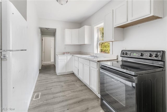 kitchen featuring light hardwood / wood-style floors, black electric range oven, white cabinetry, and sink