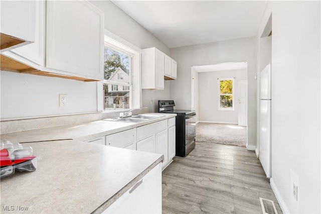 kitchen with black electric range oven, white cabinets, sink, light hardwood / wood-style floors, and white fridge