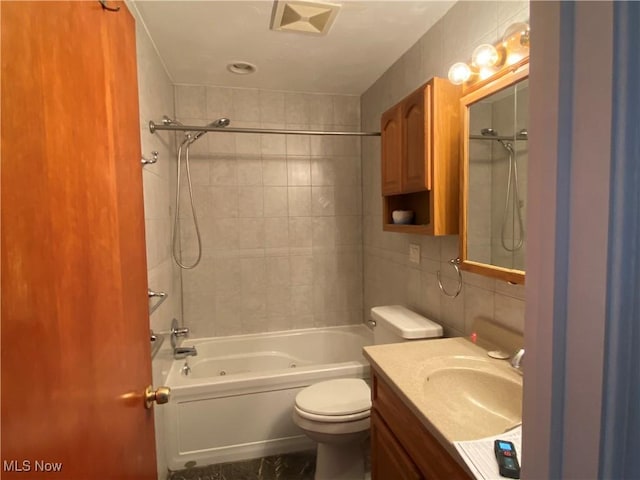 full bathroom featuring tiled shower / bath, vanity, toilet, and tile walls