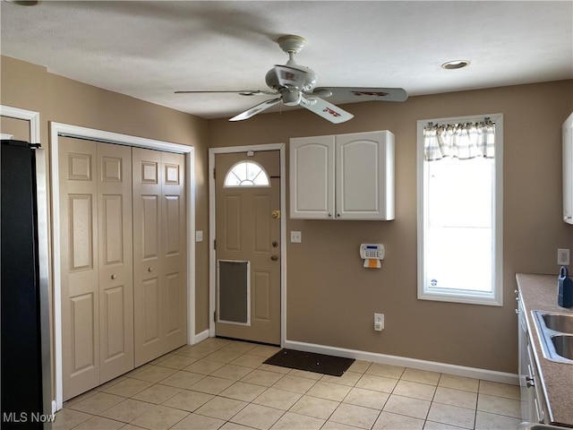 kitchen featuring ceiling fan, sink, light tile patterned floors, white cabinetry, and stainless steel refrigerator