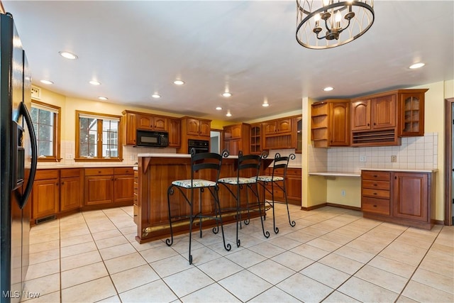 kitchen with a kitchen bar, black appliances, light tile patterned floors, a chandelier, and a center island