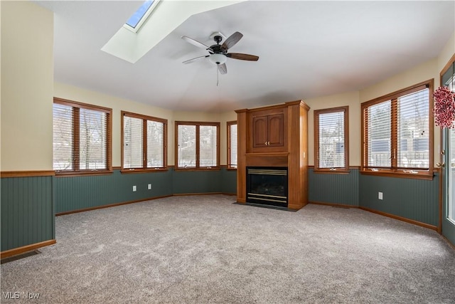 unfurnished living room with ceiling fan, a fireplace, light carpet, and a skylight