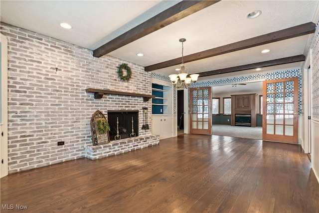 unfurnished living room featuring built in shelves, dark wood-type flooring, beamed ceiling, a fireplace, and a chandelier