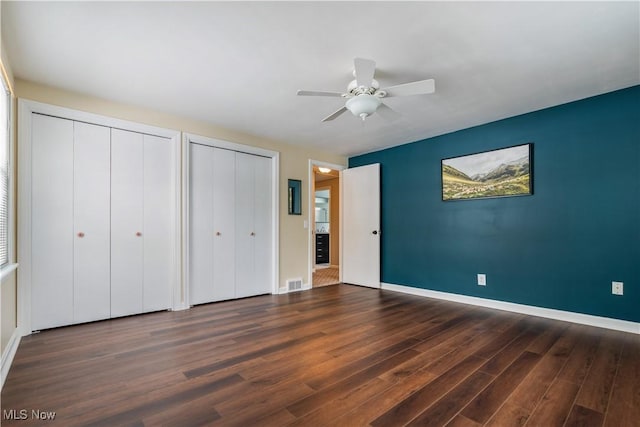 unfurnished bedroom with dark hardwood / wood-style flooring, two closets, and ceiling fan