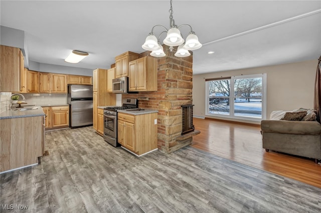 kitchen with decorative backsplash, appliances with stainless steel finishes, sink, light hardwood / wood-style flooring, and hanging light fixtures