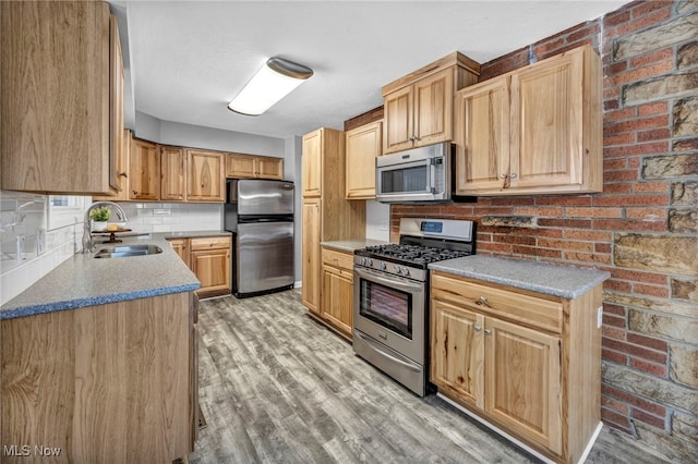 kitchen featuring appliances with stainless steel finishes, backsplash, brick wall, sink, and light hardwood / wood-style flooring