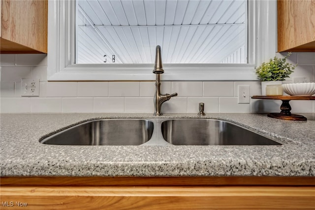 interior details featuring tasteful backsplash, light brown cabinetry, light stone counters, and sink