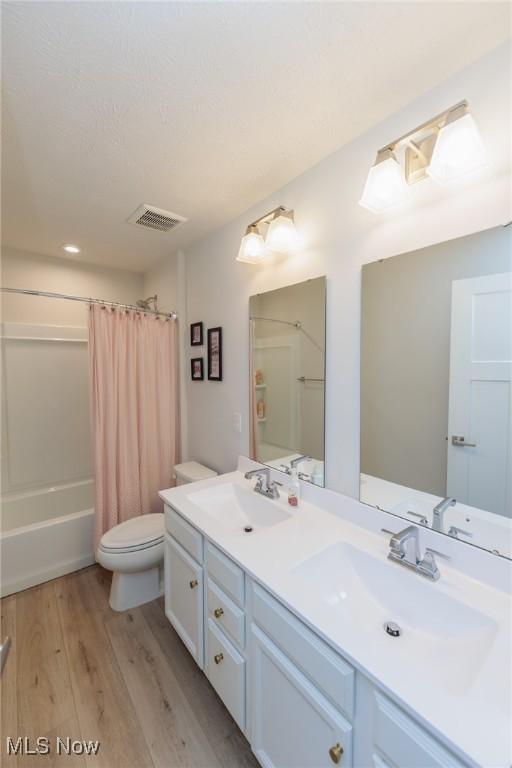 full bathroom featuring hardwood / wood-style floors, vanity, shower / bath combination with curtain, and toilet