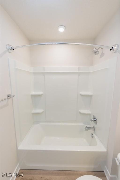 bathroom with hardwood / wood-style flooring, toilet, and washtub / shower combination