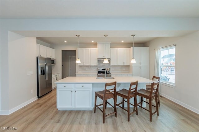 kitchen featuring tasteful backsplash, stainless steel appliances, sink, white cabinets, and hanging light fixtures