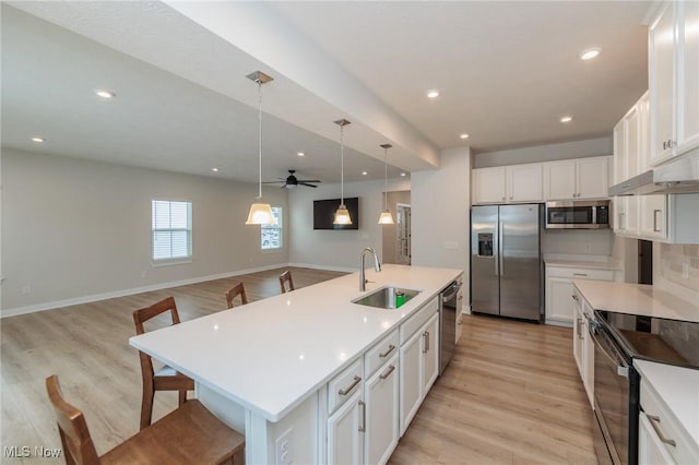 kitchen with a breakfast bar, a kitchen island with sink, white cabinets, sink, and stainless steel appliances