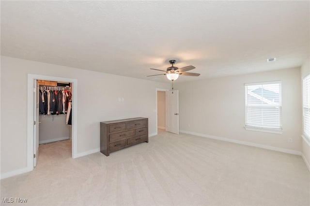 unfurnished bedroom with ceiling fan, a spacious closet, light carpet, and a closet