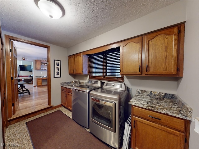 clothes washing area with cabinets, independent washer and dryer, a textured ceiling, and sink