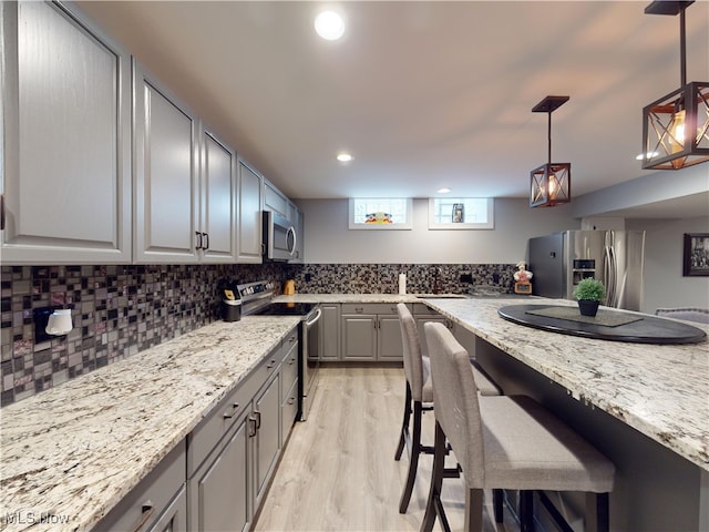 kitchen with appliances with stainless steel finishes, light stone counters, gray cabinetry, decorative light fixtures, and light hardwood / wood-style floors