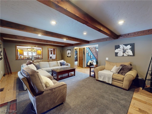 living room with beam ceiling, an inviting chandelier, and light wood-type flooring