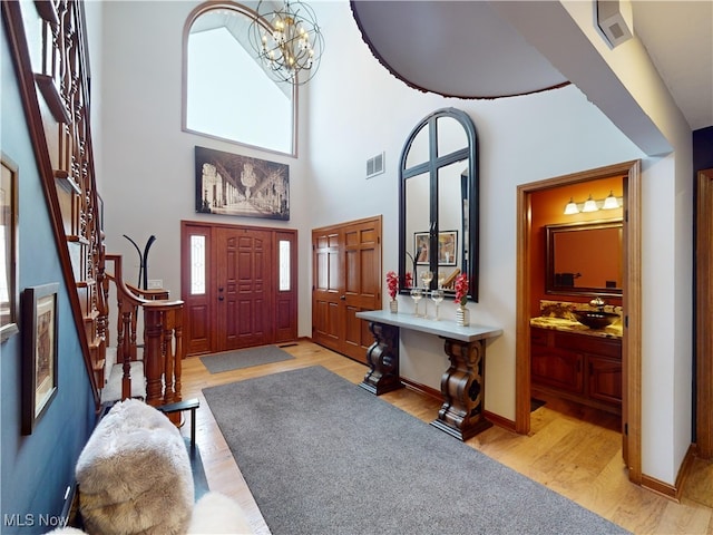 entryway featuring a towering ceiling, light wood-type flooring, and an inviting chandelier