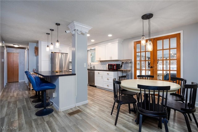 kitchen featuring white cabinetry, hanging light fixtures, stainless steel appliances, light hardwood / wood-style flooring, and decorative backsplash