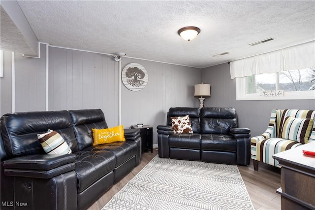 living room with a textured ceiling, wooden walls, and light hardwood / wood-style flooring