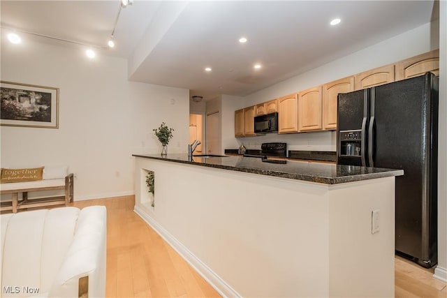 kitchen featuring rail lighting, black appliances, light hardwood / wood-style floors, dark stone counters, and sink