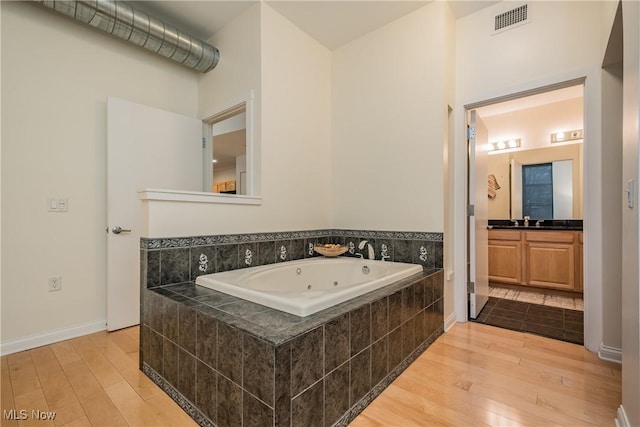 bathroom with hardwood / wood-style floors, tiled bath, and vanity