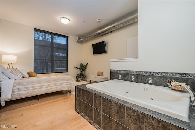 bathroom with toilet, tiled bath, and hardwood / wood-style flooring