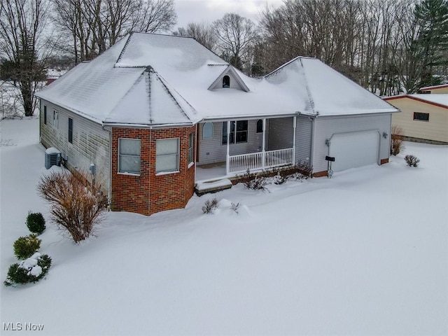 snow covered house featuring covered porch and a garage