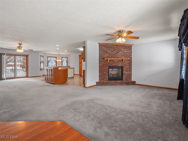 unfurnished living room with a textured ceiling, ceiling fan, light colored carpet, and a brick fireplace