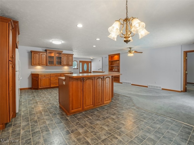 kitchen featuring decorative light fixtures, a center island with sink, a textured ceiling, ceiling fan with notable chandelier, and white refrigerator