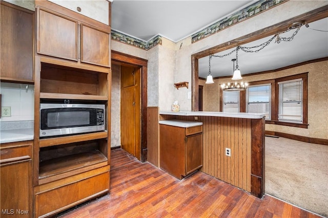 kitchen with dark wood-type flooring, an inviting chandelier, kitchen peninsula, crown molding, and pendant lighting