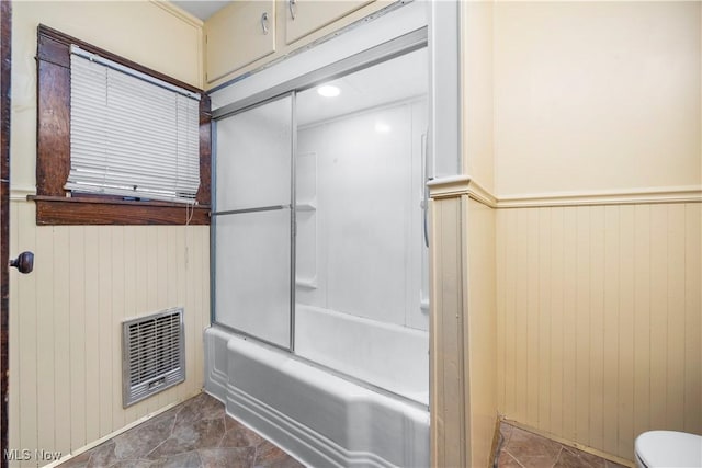 bathroom with toilet, shower / bath combination with glass door, and wooden walls