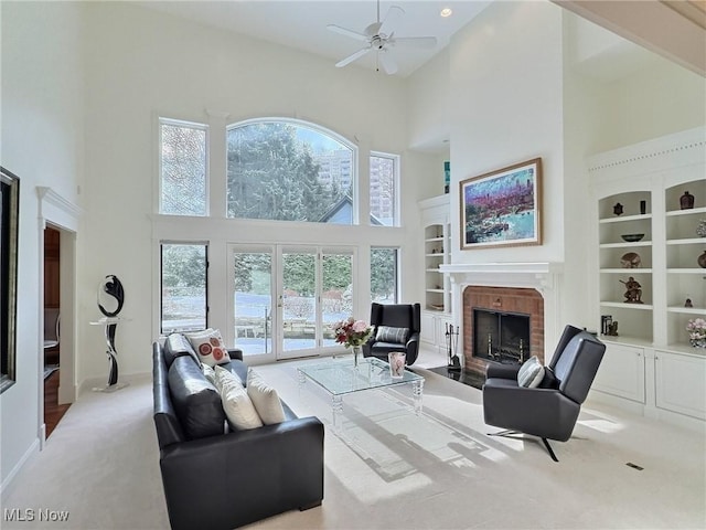 living room with a high ceiling, a brick fireplace, ceiling fan, built in features, and light colored carpet