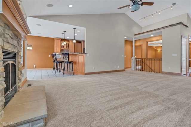 living room featuring a stone fireplace, light carpet, ceiling fan, and high vaulted ceiling