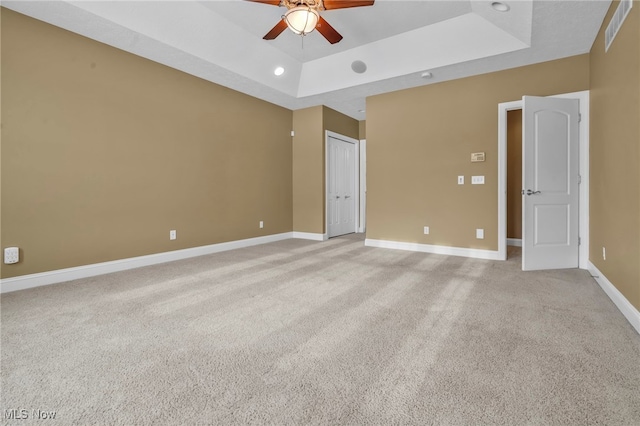 carpeted spare room with a tray ceiling and ceiling fan