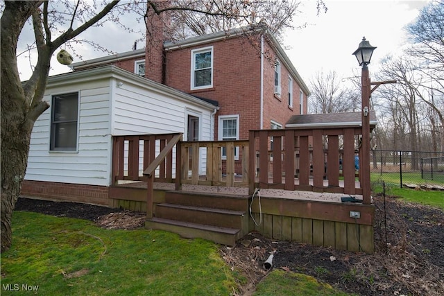 rear view of property featuring brick siding, fence, a lawn, and a wooden deck