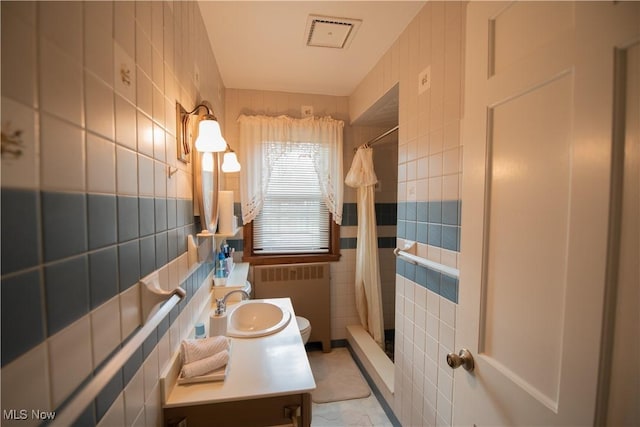 bathroom featuring radiator, visible vents, and tile walls