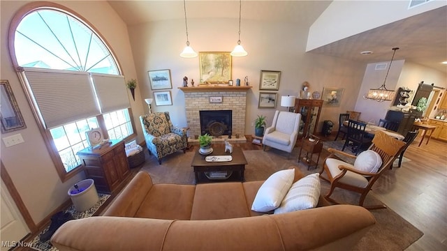 living room with vaulted ceiling, wood-type flooring, a notable chandelier, and a brick fireplace