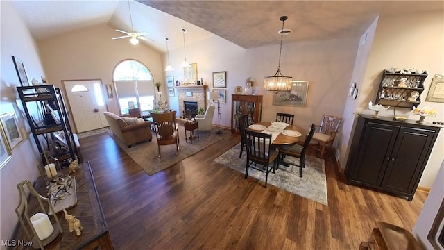 dining room with vaulted ceiling, wood-type flooring, ceiling fan with notable chandelier, and a brick fireplace