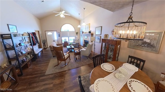 dining area with dark hardwood / wood-style floors, lofted ceiling, a fireplace, and ceiling fan with notable chandelier