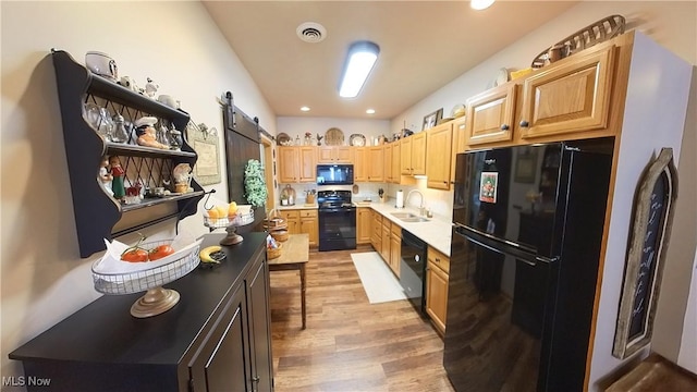 kitchen featuring a barn door, sink, black appliances, and hardwood / wood-style flooring