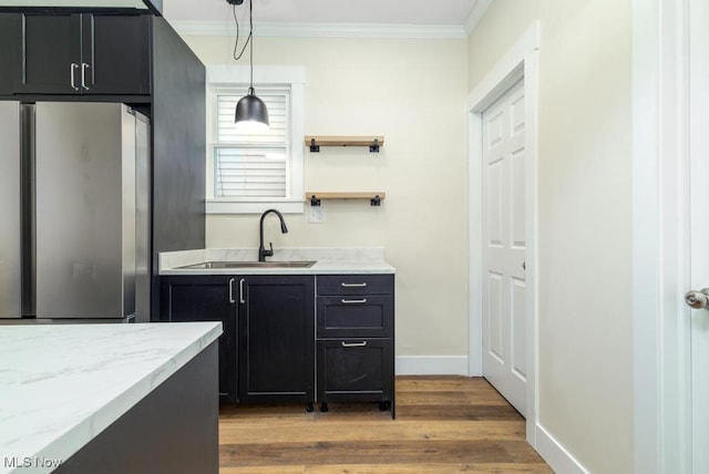 kitchen featuring hanging light fixtures, sink, light hardwood / wood-style flooring, ornamental molding, and stainless steel refrigerator