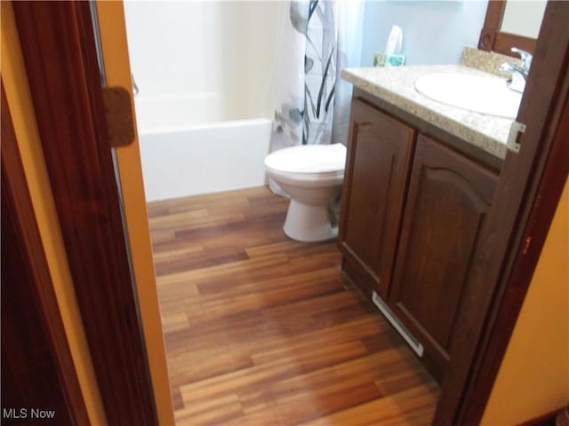 bathroom with toilet, wood finished floors, vanity, and shower / bathtub combination with curtain