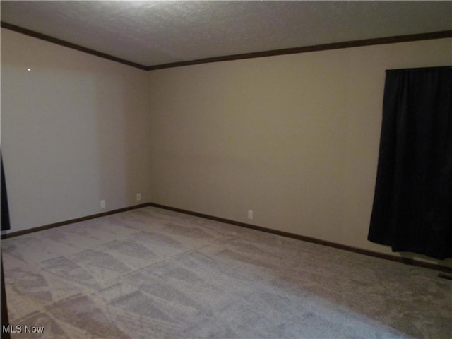 spare room with baseboards, ornamental molding, a textured ceiling, and light colored carpet