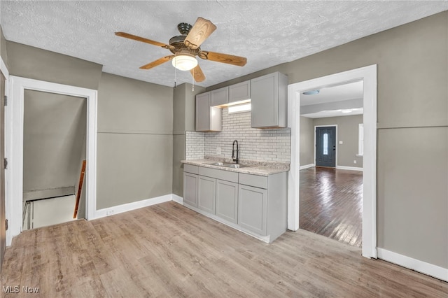 kitchen featuring backsplash, a textured ceiling, sink, light hardwood / wood-style flooring, and gray cabinets