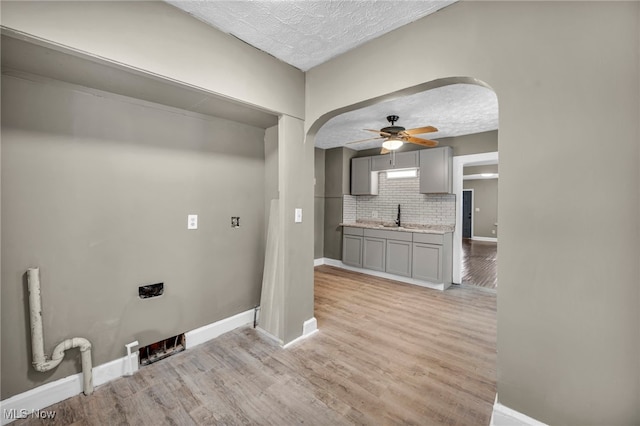 clothes washing area with light wood-type flooring, a textured ceiling, ceiling fan, and sink