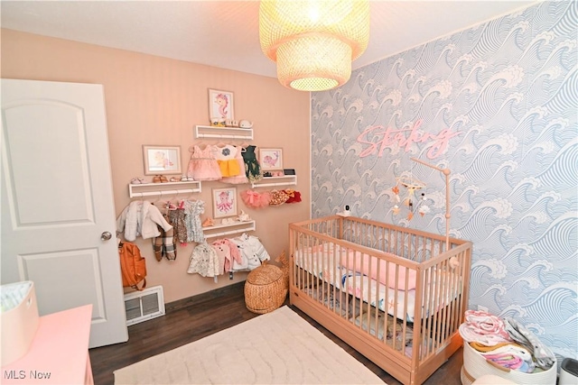 bedroom with a crib and dark wood-type flooring