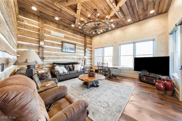 living room with log walls, beamed ceiling, a notable chandelier, a towering ceiling, and hardwood / wood-style flooring