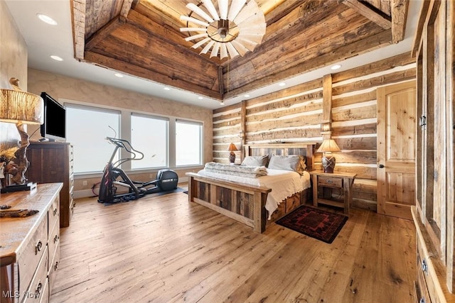 bedroom featuring a raised ceiling, rustic walls, a chandelier, and light wood-type flooring