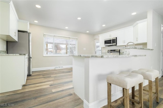 kitchen featuring white cabinetry, light hardwood / wood-style flooring, kitchen peninsula, a kitchen bar, and appliances with stainless steel finishes